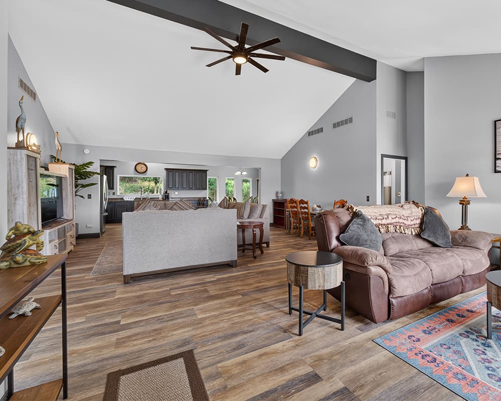 Open-concept living area with a cozy sofa, wooden flooring, and a modern kitchen in the background.